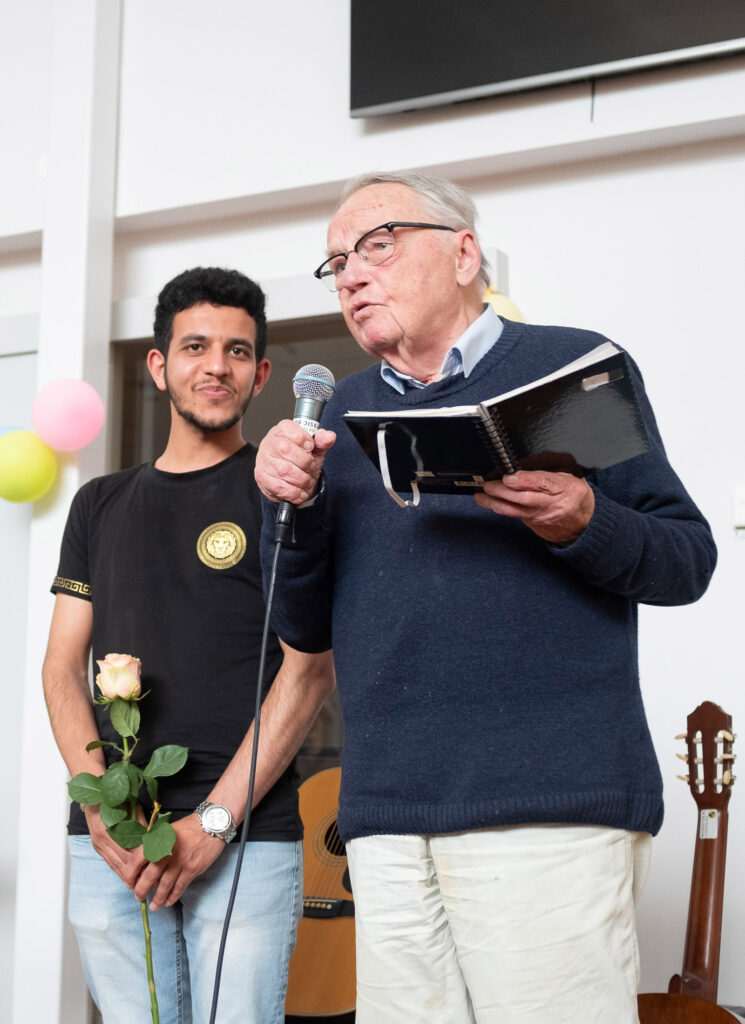 Nils Zandhers presenterar årets mottagare av Nisse-stipendiet. Han håller i en mikrofon i ena handen och i en bok i andra.